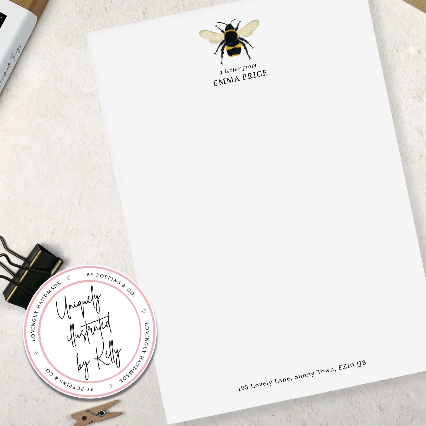 A single sheet of personalised bumblebee writing paper. The writing paper is white and has an illustration of a bee at the top of the page. Italic script reads 'a letter from' with the name 'Emma Price' typed in all caps font below it. At the bottom of the page is a typed address.