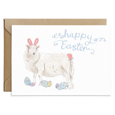 A funny Easter Greetings Card featuring a sheep wearing pink easter bunny ears and a pink bunny tail. Patsel coloured pattern easter eggs are scattered below the sheets feet. Pink and blue scripted writing above reads 'Happy Easter'. White background greetings card with a brown Kraft envelope laying behind. Greetings card by Poppins and Co.