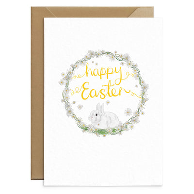 A cute easter greetings card featuring bunny drawn inside a wreath of daisies and completed by hand scripted yellow text that reads 'happy easter'. 6 white greetings cards laid out on top of 6 brown recycled envelopes. Greetings cards by Poppins and co.