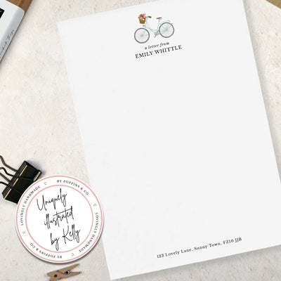 A single sheet of personalised bicycle writing paper. The writing paper is white and has an illustration of a bicycle with flowers in the basket at the top of the page. Italic script reads 'a letter from' with the name 'Emily Whittle' typed in all caps font below it. At the bottom of the page is a typed address.