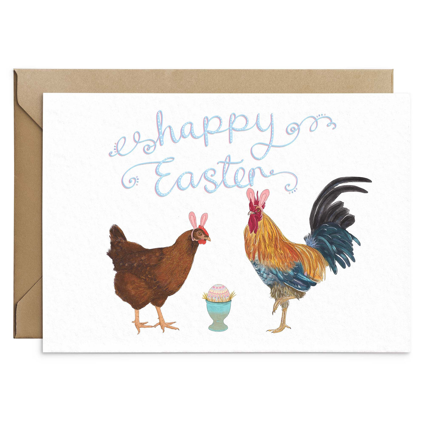A funny Easter Greetings Card featuring a hen and a cockerel wearings pink easter bunny ears. A pastel patterned egg sits in a blue egg cup in the middle of them. Pink and blue scripted writing above reads 'Happy Easter'. White background greetings card with a brown Kraft envelope laying behind. Greetings card by Poppins and Co.