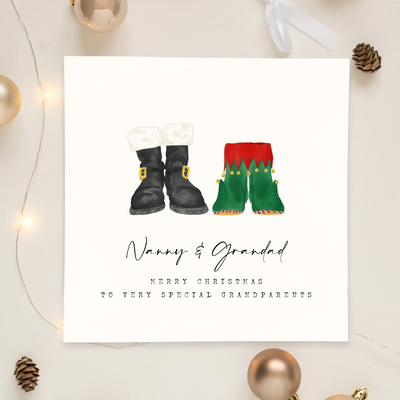 A square christmas card for grandparents featuring unique watercolour illustrations of a pair of Santa boots and elf boots side beside. Beneath the boots personalised text reads 'Nanny and Grandad - merry christmas to very special grandparents.'