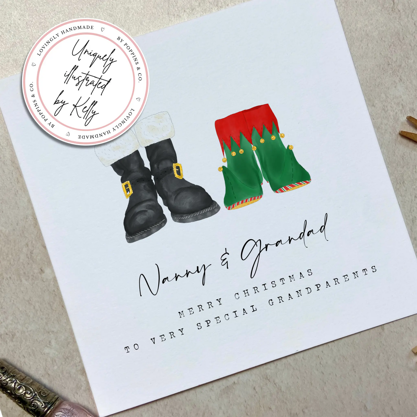 A square christmas card for grandparents featuring unique watercolour illustrations of a pair of Santa boots and elf boots side beside. Beneath the boots personalised text reads 'Nanny and Grandad - merry christmas to very special grandparents.'