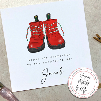 A personalised square greetings card featuring a unique illustration of christmas themed red boots and personalisable text reading 'happy 1st christmas to our wonderful son, Jacob'.