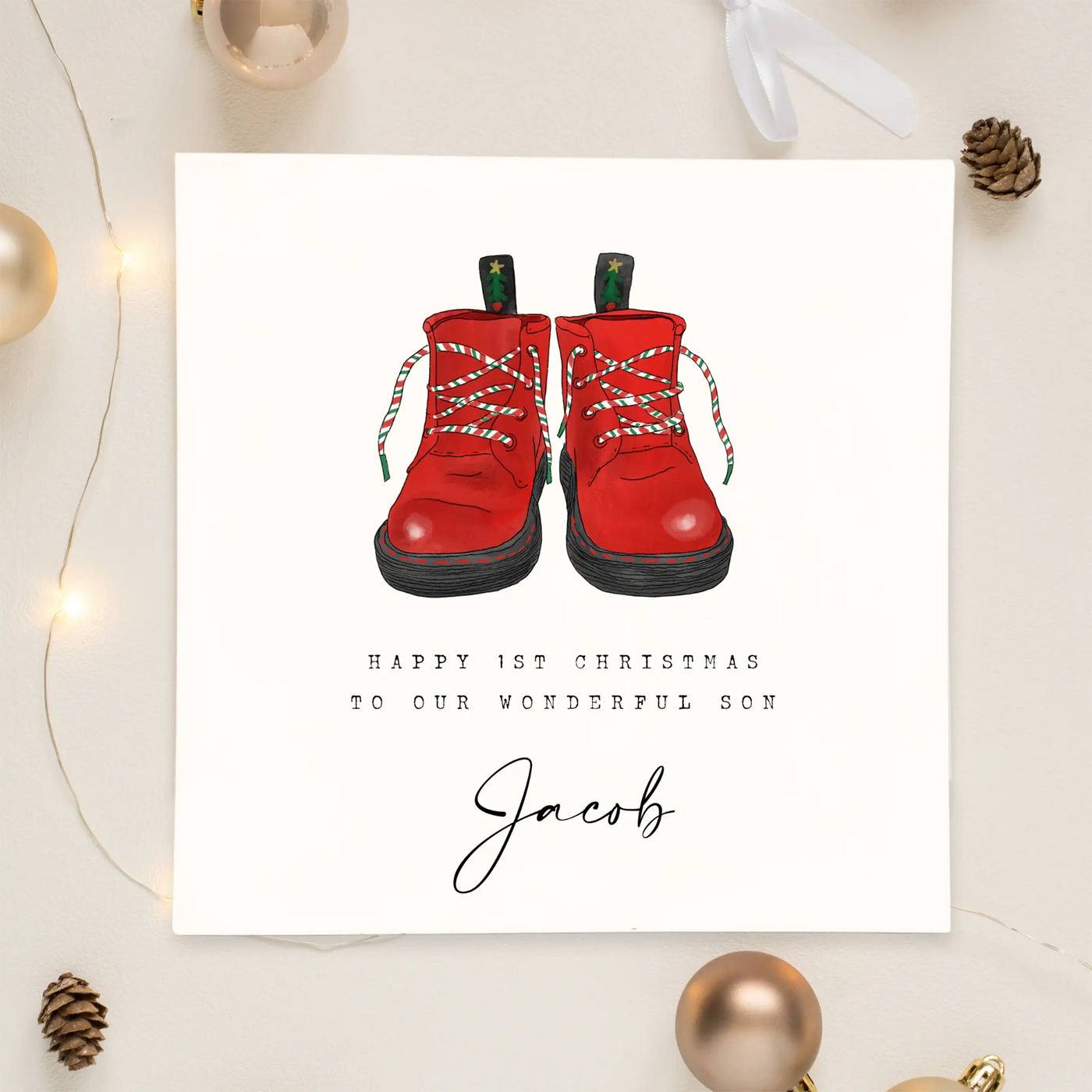 A personalised square greetings card featuring a unique illustration of christmas themed red boots and personalisable text reading 'happy 1st christmas to our wonderful son, Jacob'.