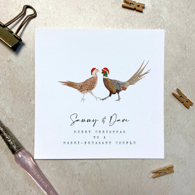 A square christmas card for a magnificent couple featuring unique watercolour illustrations of a pair of pheasants in christmas hats. Beneath the birds personalised text reads 'Sammy and Dave- merry Christmas to a magni-pheasant couple'