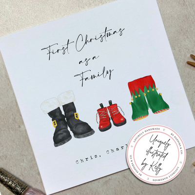 A square christmas card for their first christmas as a family - featuring unique watercolour illustrations of a pair of Santa boots and elf boots side beside, with baby christmas boots in-between. Personalised text reads 'First Christmas as a Family - Chris, Charli and Max' 