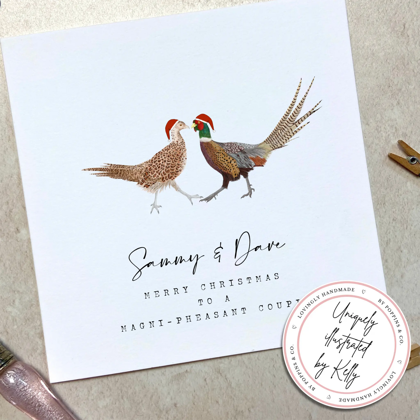 A square christmas card for a magnificent couple featuring unique watercolour illustrations of a pair of pheasants in christmas hats. Beneath the birds personalised text reads 'Sammy and Dave- merry Christmas to a magni-pheasant couple'