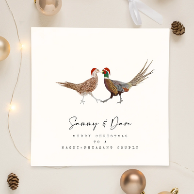 A square christmas card for a magnificent couple featuring unique watercolour illustrations of a pair of pheasants in christmas hats. Beneath the birds personalised text reads 'Sammy and Dave- merry Christmas to a magni-pheasant couple'