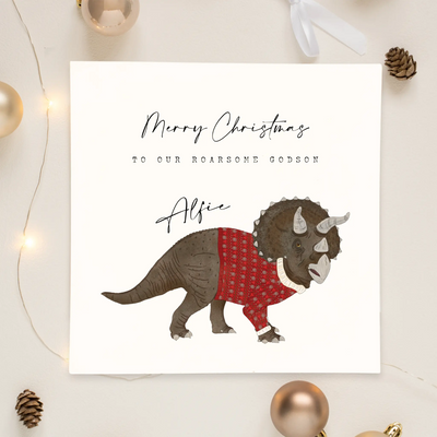 A personalised square greetings card featuring a unique illustration of triceratops in a christmas jumper and personalisable text reading 'Merry Christmas to our roar some godson Alfie'.