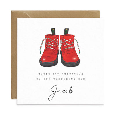 A personalised square greetings card featuring a unique illustration of christmas themed red boots and personalisable text reading 'happy 1st christmas to our wonderful son, Jacob'.