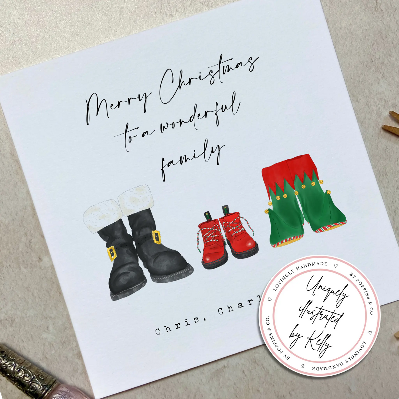 A square christmas card for a wonderful family - featuring unique watercolour illustrations of a pair of Santa boots and elf boots side beside, with baby christmas boots in-between. Personalised text reads 'Merry Christmas to a wonderful family - Chris, Charli and Max' 