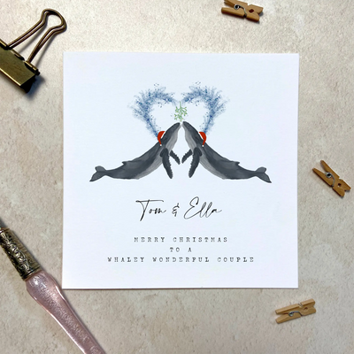 A square christmas card for a wonderful couple featuring unique watercolour illustrations of a pair of humpback whales in christmas hats. Beneath the birds personalised text reads 'Tom and Ella - merry Christmas to a whaley wonderful couple'