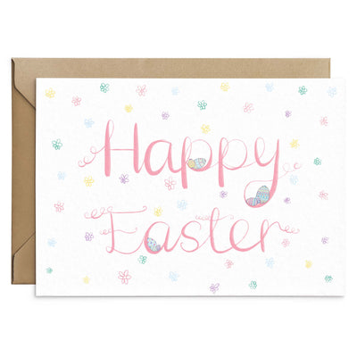 A pink easter card design with scripted text and illustrations of pastel coloured  easter eggs. White card on top of a brown recycled envelope. Easter Card by Poppins and co.