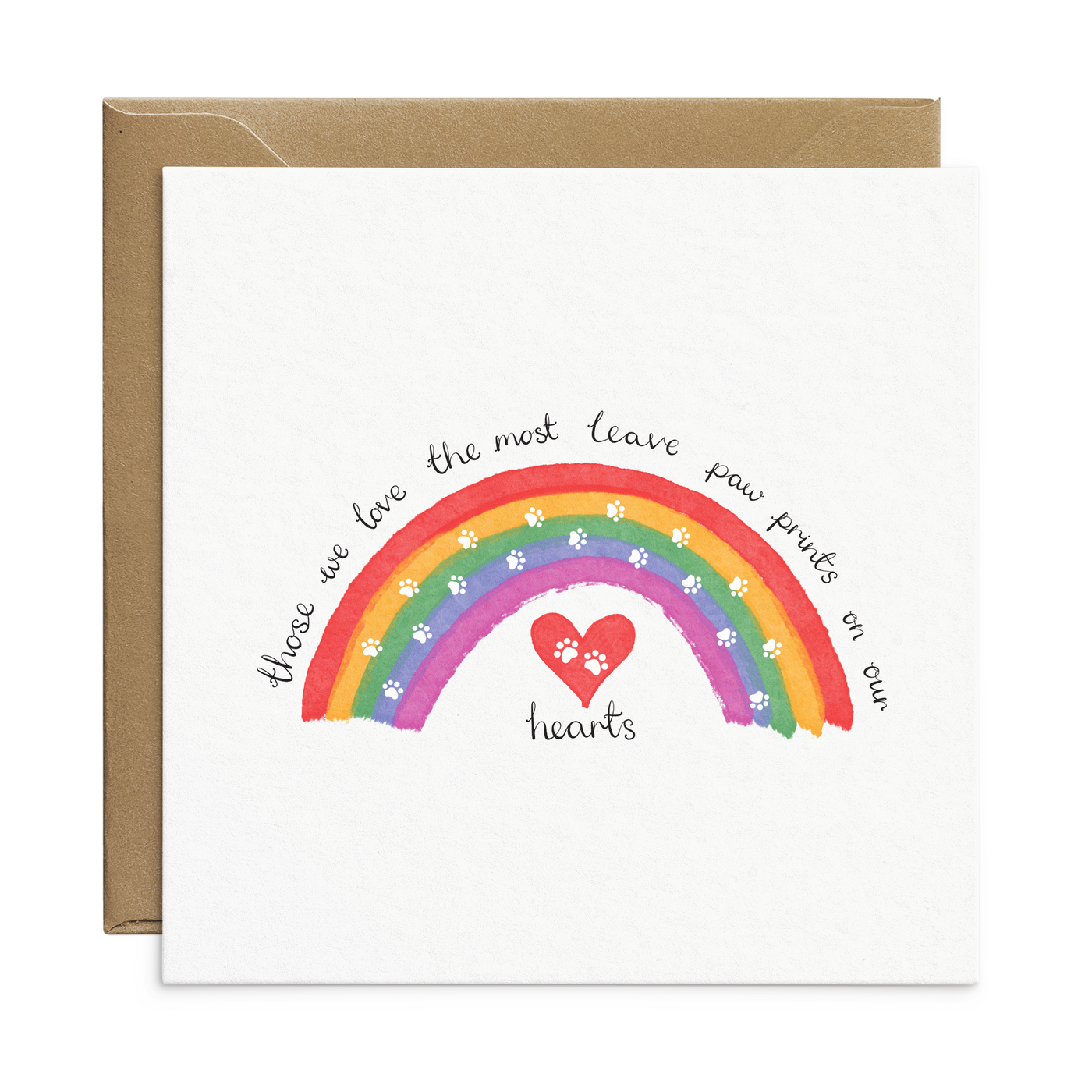 A square white card featuring a colourful rainbow with white paw prints and a red heart. Text reads 'the ones we love the most leave paw prints on our hearts'. Placed behind the card is a recycled brown envelope. Pet Sympathy Card from Poppins and Co.