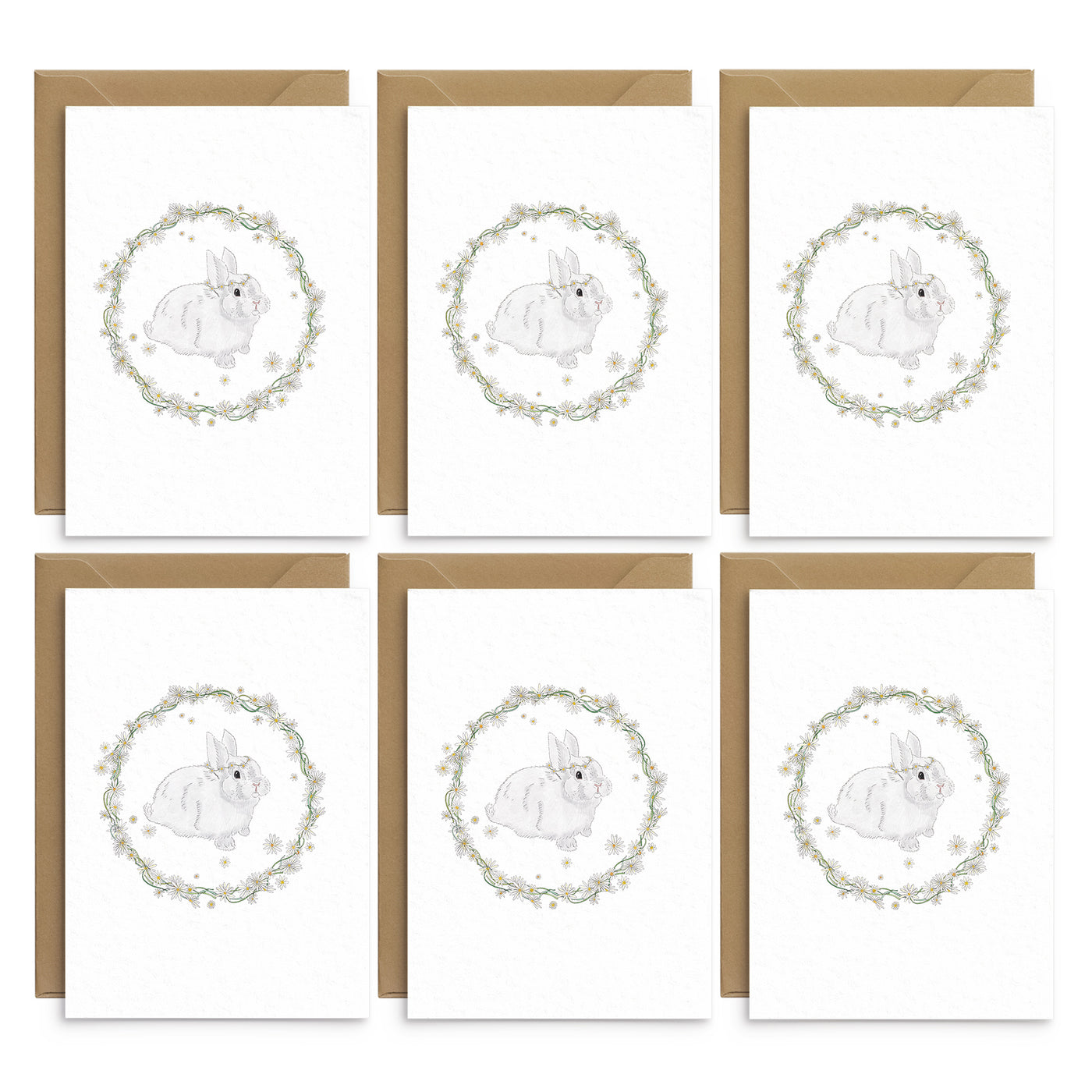 A set of 6 spring themed greetings cards featuring a white bunny wearing a daisy crown pictured inside a rather made of daisies and greenery. No text. Photo shows 6 cards laid out on top of recycled brown envelopes. Easter greetings cards by Poppins and co.