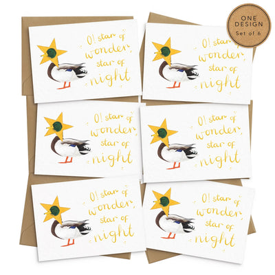 A unique set of 6 christmas cards lay on a a white background with 6 brown envelopes. The card depicts a whimsical illustration of cute duck with a star costume around its head.  Hand scripted yellow text reads 'O! star of wonder, star of night'.