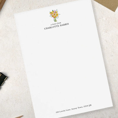 A single sheet of personalised sunflower letter writing paper by Poppins and co. The writing paper is white and has a small bunch of yellow sunflowers illustrated at the top of the page. Italic script reads 'a letter from' with the name 'Charlotte Harris' typed in all caps font below it. At the bottom of the page is a typed address.