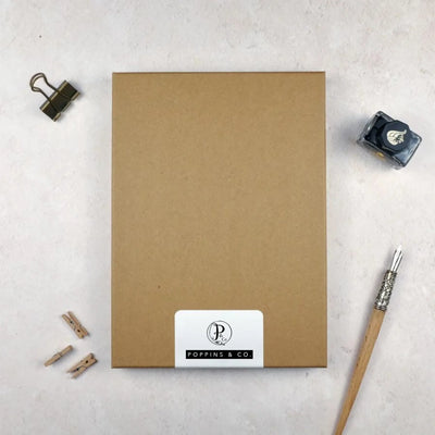 A luxury brown stationery gift box by poppins and co surrounded by writing equipment. A white label on the box shows the Poppins and co logo.