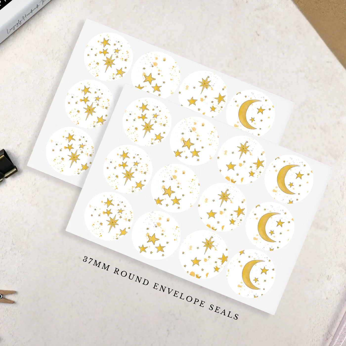 Two sheets of gold star and moon patterned 37mm round envelope seals on a light surface.