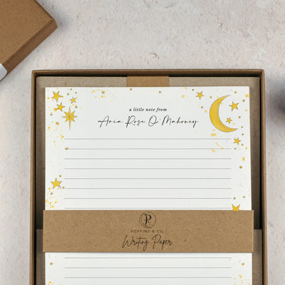 A celestial themed lined writing paper set by in a brown kraft luxury gift box. The writing paper is white and has illustrations of a yellow stars and moons around the border. Italic script reads 'a little note from' with the name 'Aria Rose O'Mahoney' typed in in a script font. 