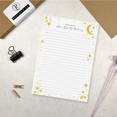 A single sheet of lined A5 writing paper with star and moon design on a light surface with stationery items.