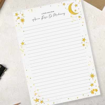 A single sheet of lined A5 writing paper with star and moon design on a light surface with stationery items.