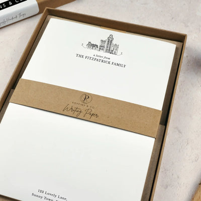A family writing paper set by in a brown kraft luxury gift box. The writing paper is white and has illustrations of a little line drawn houses in black at the top of the page. Italic script reads 'a letter from' with 'The Fitzpatrick Family' typed in all caps font below it. 