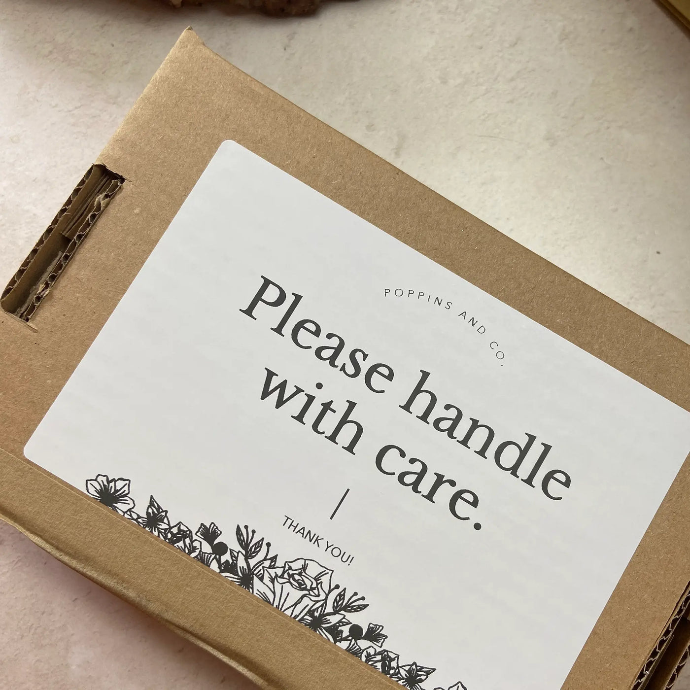 A white please handle with care label on a brown postage box from Poppins and Co