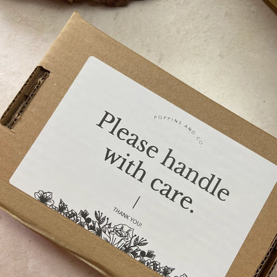 A white please handle with care label on a brown postage box from Poppins and Co