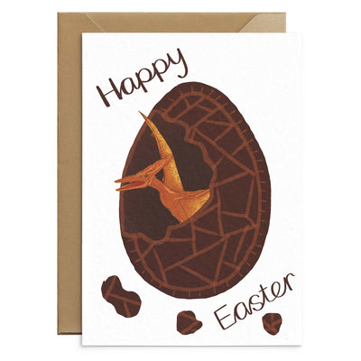 An unusual easter card for kids featuring a orange pterodactyl hatching from inside chocolate easter egg. Brown text reads 'happy easter'. Illustration on white A6 card with recycled envelopes. Easter cards by Poppins and co.