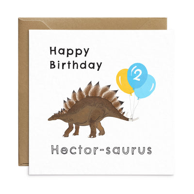 A personalised kids dinosaur birthday card with unique illustration of a stegosaurus with a bunch of balloons tied to its tail. Personalised text reads 'Happy Birthday Hector-saurus' with the number '2' on the balloons. Square card with brown Kraft envelope. Kids Birthday Card by Poppins and co.