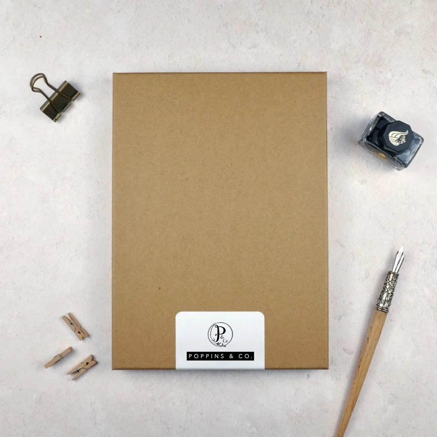 A luxury brown stationery gift box by poppins and co surrounded by writing equipment. A white label on the box shows the Poppins and co logo.