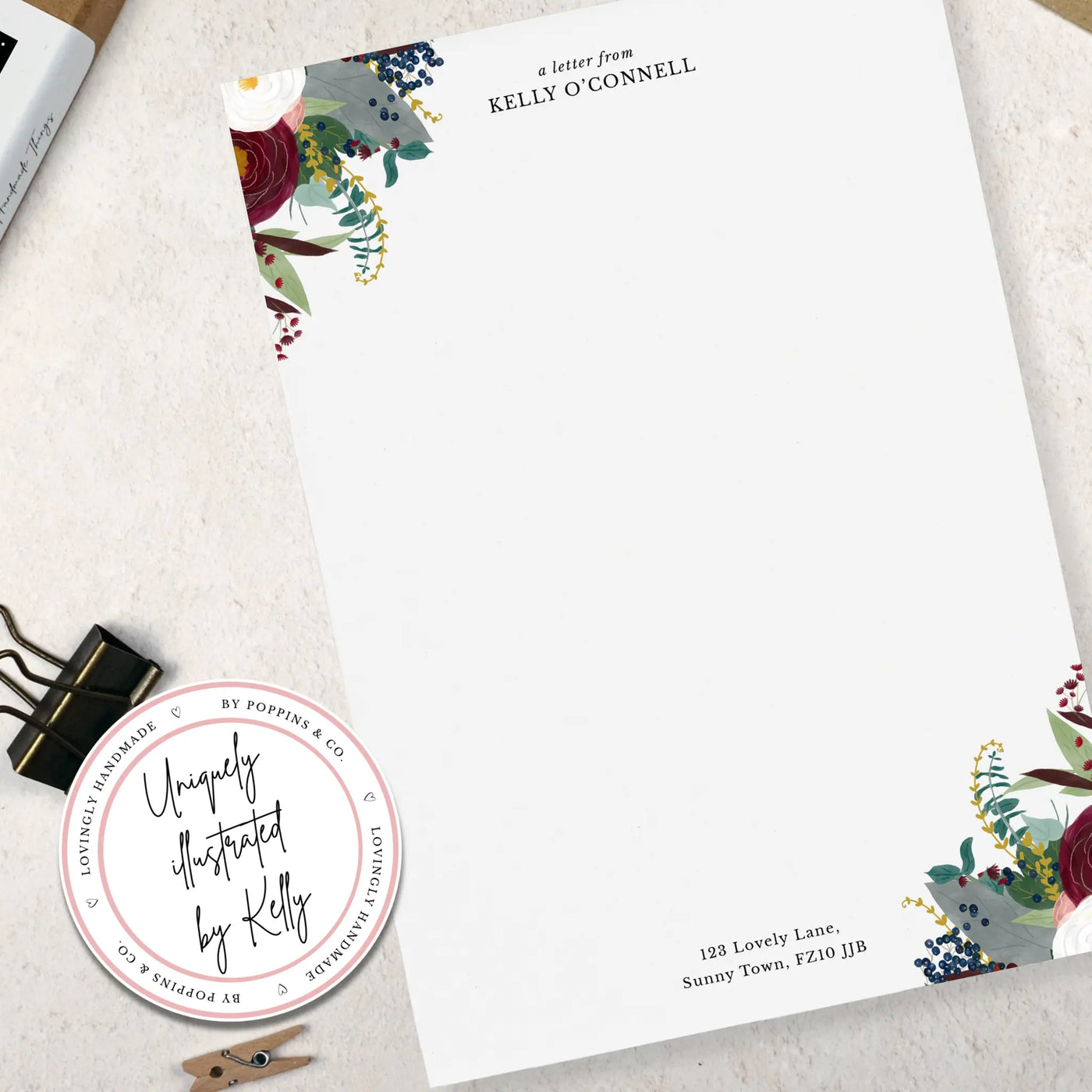 A single sheet of winter floral themed writing paper. The writing paper is white and has illustrations of a burgundy and white flowers and foliage on two corners. Italic script reads 'a letter from' with a name typed in all caps font below it and a address at the bottom of the paper.