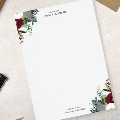 A single sheet of winter floral themed writing paper. The writing paper is white and has illustrations of a burgundy and white flowers and foliage on two corners. Italic script reads 'a letter from' with a name typed in all caps font below it and a address at the bottom of the paper.
